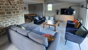 Een woonkamer met een stenen muur, een eethoek, een bank, een salontafel en een televisie.