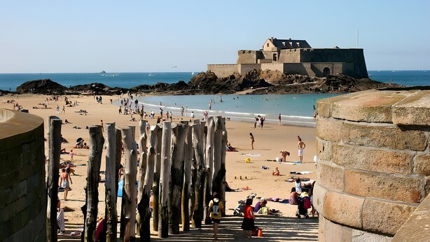 Een strand met mensen, een kasteelachtig gebouw en een heldere lucht.