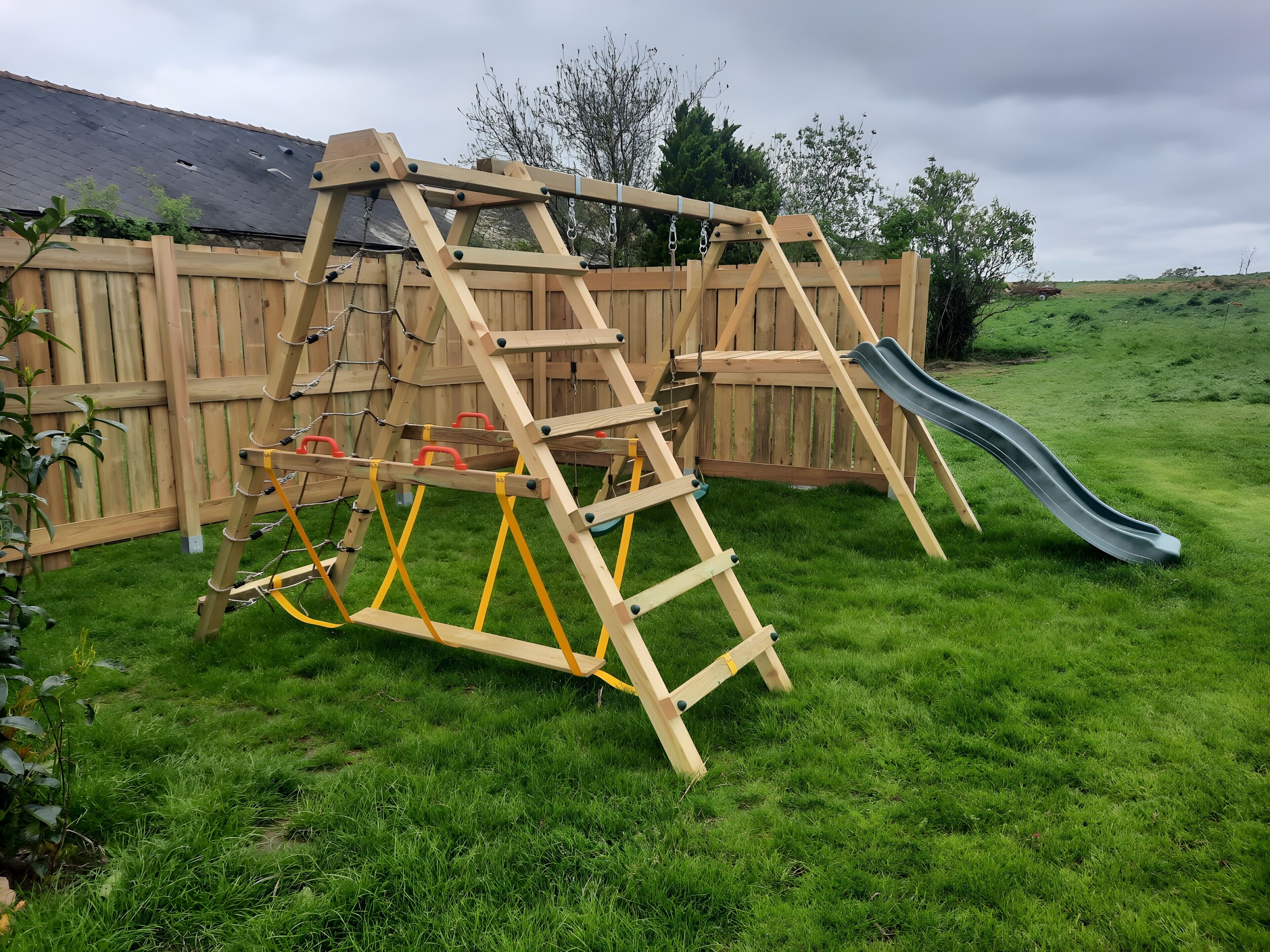 Estructura de madera para juegos con un tobogán y una escalera de cuerda en un jardín césped.