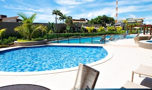 Uma piscina com espreguiçadeiras, palmeiras e um edifício ao fundo.