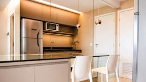 Une cuisine moderne dotée d’appareils électroménagers en acier inoxydable, d’un îlot central en verre et de chaises blanches.