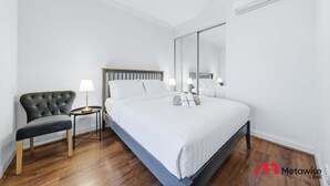Una camera d'albergo moderna con un letto grande, un tavolino con una lampada, una poltrona imbottita scura e uno specchio ampio.