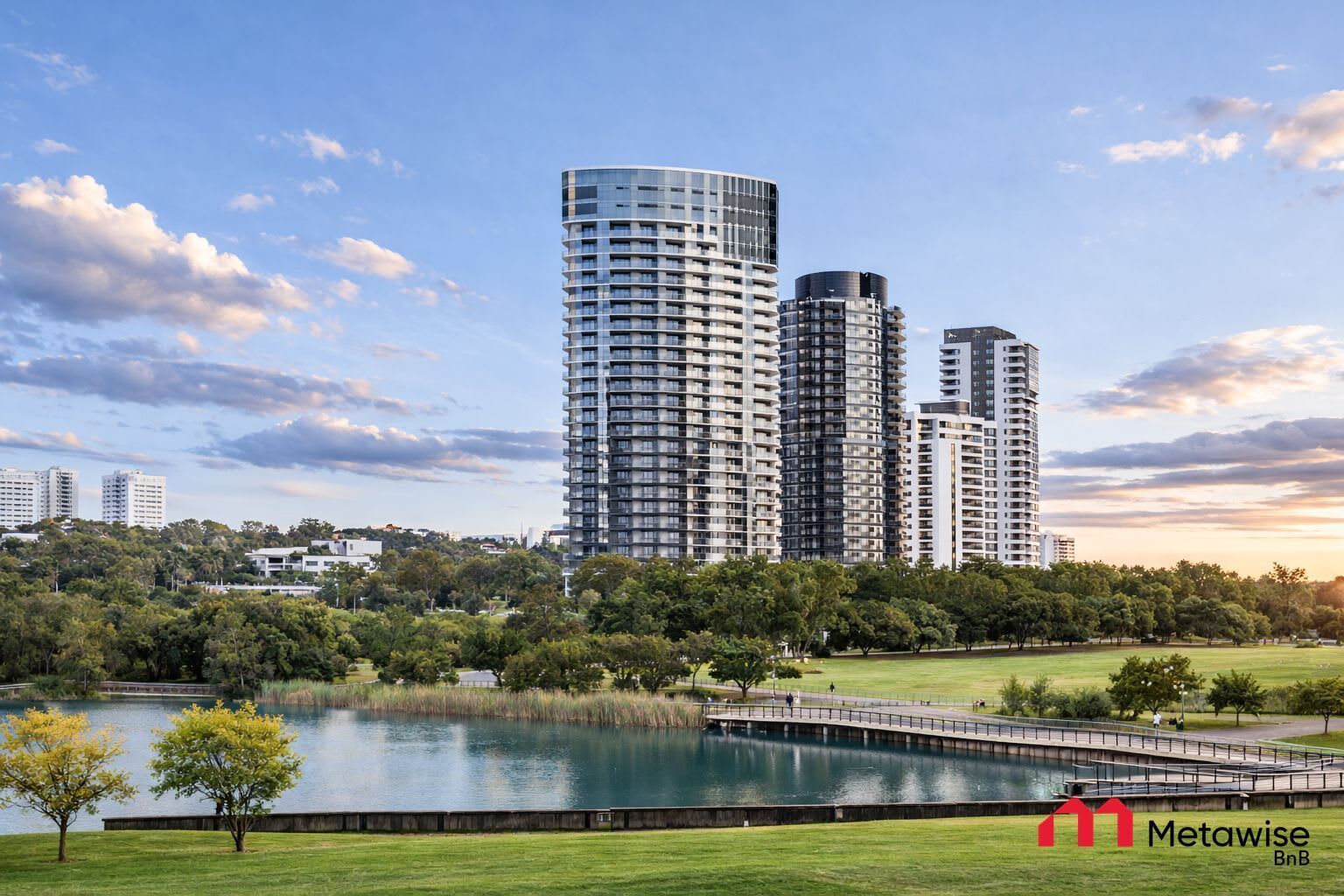 A modern high-rise building complex with a park and lake in the foreground.