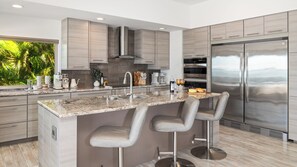 A modern kitchen with a central island, stainless steel appliances, and a view of greenery outside.
