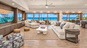 A spacious living room with a large TV, comfortable seating, and a view of the ocean.