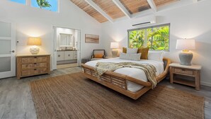 A bedroom with a large bed, a nightstand, a dresser, a chair, a window with a view of greenery, and an air conditioning unit.