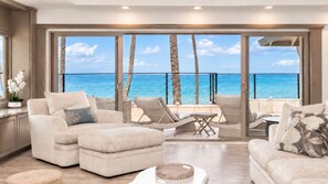 A spacious living area with a large window overlooking a beach, furnished with sofas and a table.