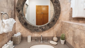 A bathroom with a round mirror, a sink, a towel rack, a basket, a soap dispenser, and a potted plant.