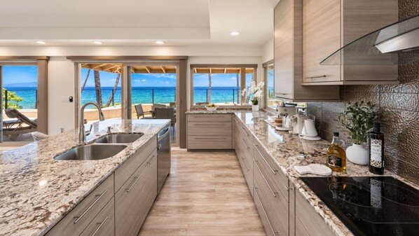A modern kitchen with a large island, granite countertops, and a view of the ocean.