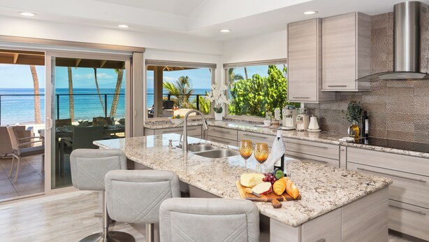 A modern kitchen with a large island, a view of the ocean, and a dining area with chairs.