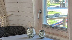 Habitación compacta con una mesa blanca, dos jarrones de vidrio, un banco gris y una ventana con vistas a un jardín.