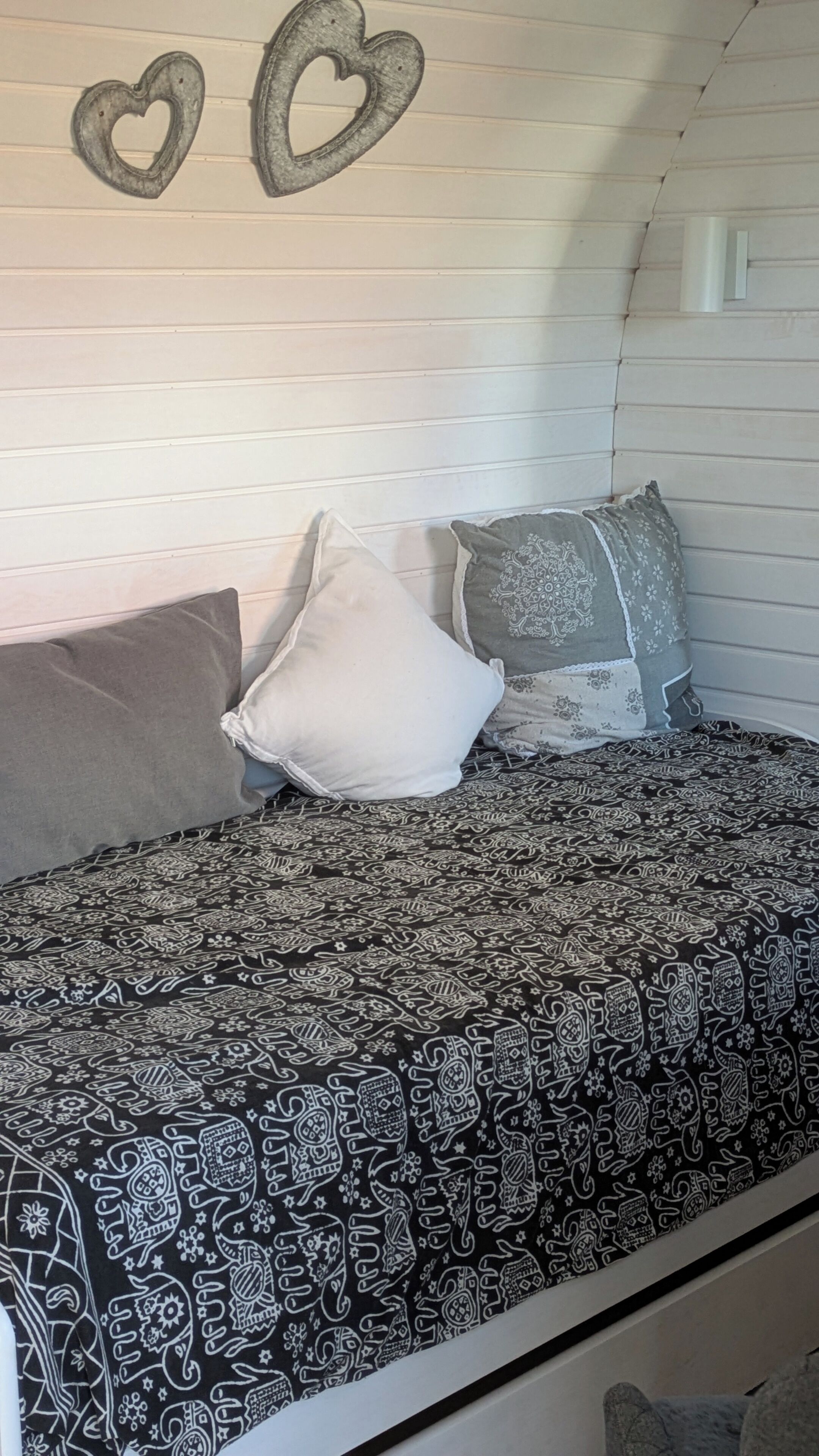 A bed with patterned bedding, two pillows, and heart-shaped wall decorations.