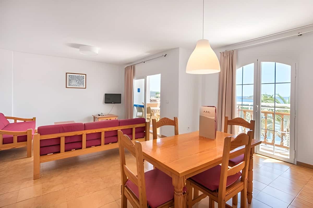 A room with a wooden dining table, red cushioned seating, a television, and a large window with a view.