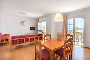 Ein Zimmer mit einem Holzesstisch, roter Polsterbank, einem Fernseher und einem großen Fenster mit Blick.