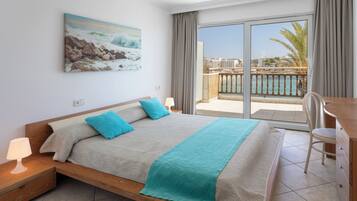Habitación de hotel con cama, mesita de noche, escritorio con silla, un cuadro en la pared y vista al mar por la ventana.