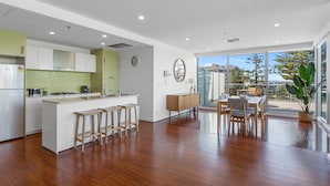 A modern kitchen with a central island, a dining area with a table and chairs, and a large window offering a view of the outdoors. - Stylish 2-bed With Terrace, 3-min Walk to Beach (Adelaide)
