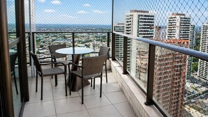 Un balcón con una mesa de vidrio y sillas de mimbre, con vistas a un paisaje urbano con rascacielos.