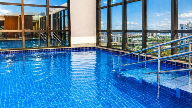 Una piscina interior con agua azul cristalina, ventanas amplias y vistas a la ciudad.