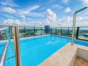 A rooftop infinity pool with a city view, metal railings, and a clear sky. - Golden Shop Home Service- Flat - Boa Viagem (Recife)