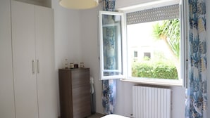 Ein Schlafzimmer mit Fenster, Heizkörper, Kleiderschrank und Nachttisch.