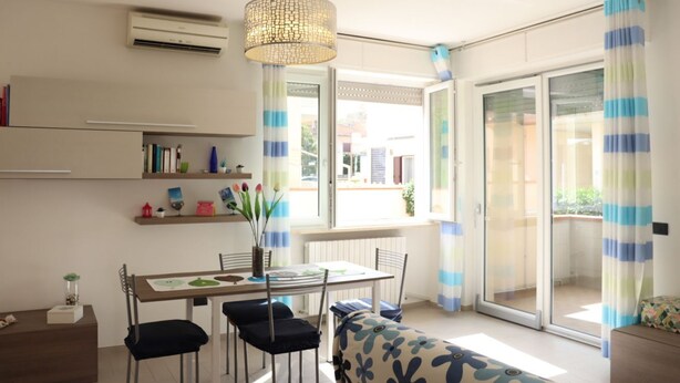 Ein modernes Wohnzimmer mit Esstisch, Stühlen, einer Couch, einer Hängeleuchte und Blick durch eine Glastür.