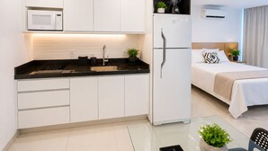 A compact kitchen with a microwave, sink, and refrigerator, adjacent to a bedroom with a bed and bedside table. - Beach Class Ilha do Leite- Flat/Studio 1105 (Ilha do Leite)