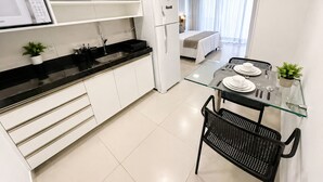 A modern kitchen with white cabinets, a black countertop, a glass dining table, and black chairs. - Beach Class Ilha do Leite- Flat/Studio 1105 (Ilha do Leite)
