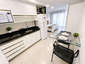 A modern kitchen with white cabinets, a black countertop, a glass dining table, and black chairs. - Beach Class Ilha do Leite- Flat/Studio 1105 (Ilha do Leite)