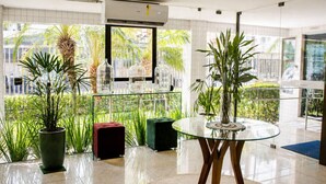 Een moderne hotel lobby met een glazen tafel, potplanten en uitzicht op groen.