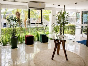 A modern hotel lobby with a glass table, potted plants, and a view of greenery outside. - Golden Home shopping 2003 Flat boa viagem (Recife)