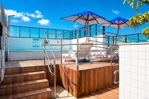 A poolside area with wooden steps, white lounge chairs, and blue umbrellas. - Golden Home shopping 2003 Flat boa viagem (Recife)