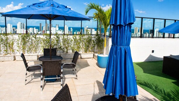 Een dakterras met uitzicht over de stad, zitplaatsen buiten en blauwe parasols.