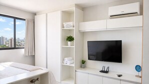 Een moderne hotelkamer met een bed, een televisie, een bureau met een computer, een raam met gordijnen en een airconditioning.