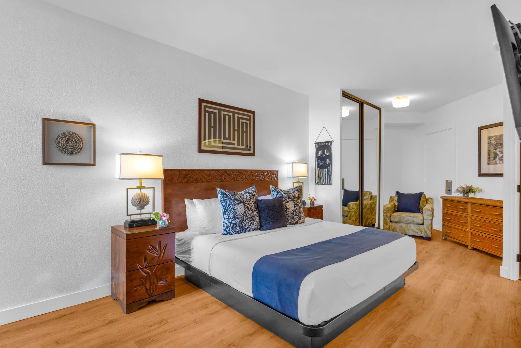 Ein Hotelzimmer mit einem großen Bett, einem Holz-Kopfstück, zwei Nachttischen mit Lampen, einem Spiegel, einem Sessel und einer Kommode.