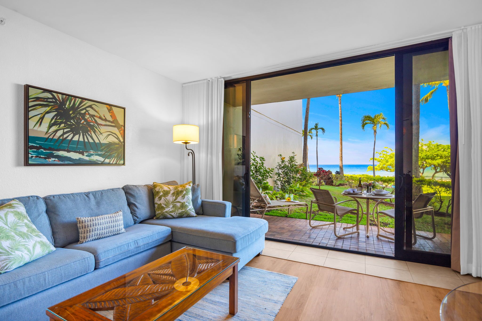 A living room with a sofa, coffee table, and a painting of a beach scene.