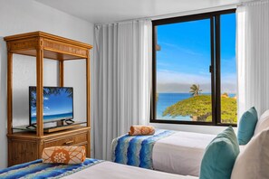 A hotel room with a television on a wooden stand, a bed with a blue patterned bedspread, and a large window with a view of the ocean. - Kaanapali Shores | Ocean View 4 BR, Sleeps 12 | Car Incl. w/ 6+ Nights | KS ML-3776 by KBM (Lahaina)