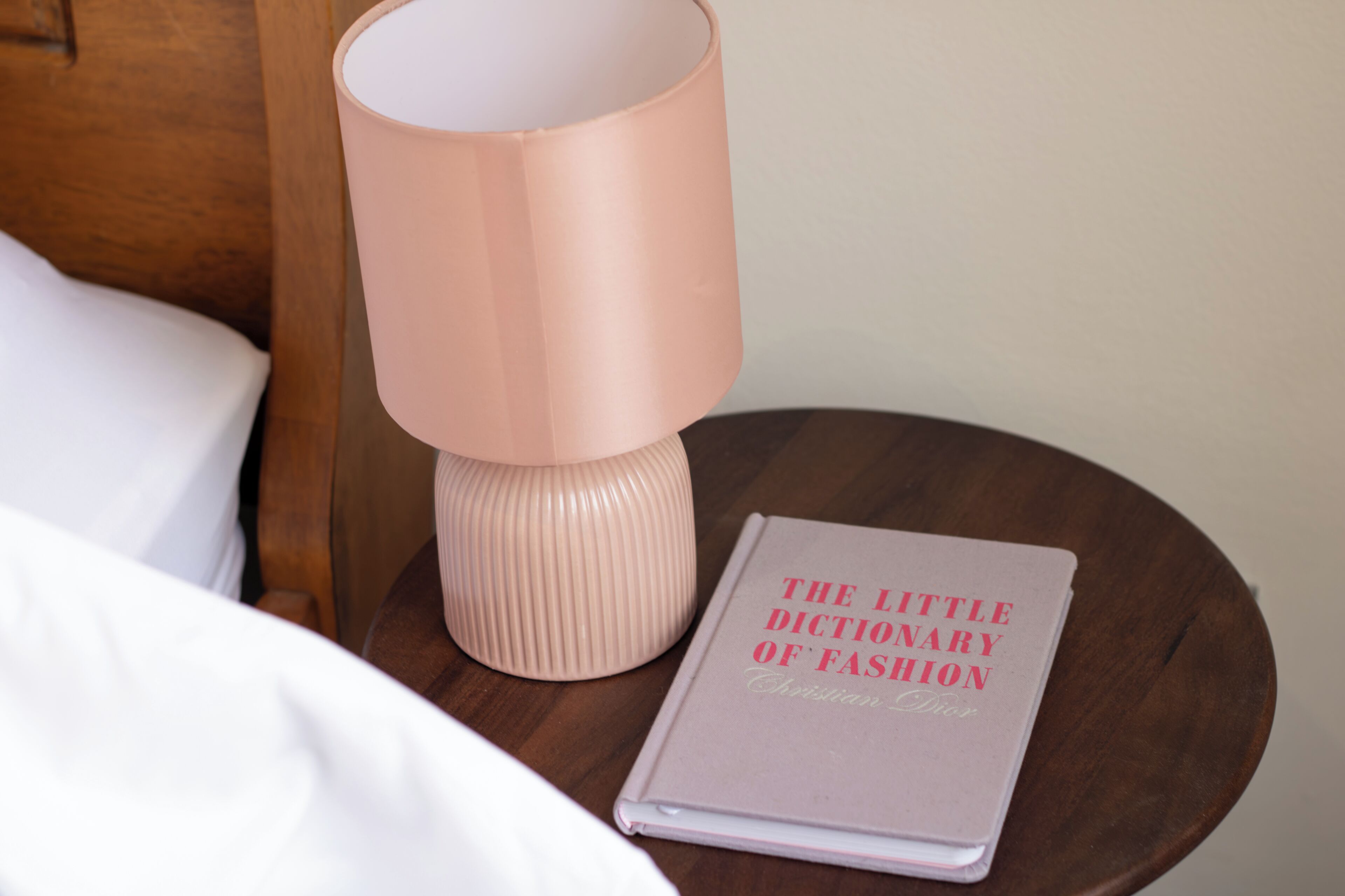 A bedside table with a lamp and a book titled 'The Little Dictionary of Fashion.'