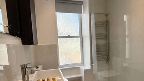 Ein modernes Badezimmer mit Duschkabine aus Glas, Waschtisch und einem Fenster für natürliches Licht.