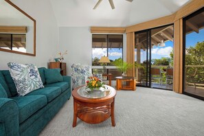 A modern living room with a teal sofa, a wooden coffee table, and a view of the outdoors through large sliding glass doors. - 2 Grand Champions | Treeline View | Sleeps 10 | Free Car w/ 6+ Nts | ML-3777 (Wailea)