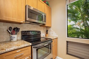 A kitchen with wooden cabinets, a stainless steel microwave, a black oven, and a granite countertop. - 2 Grand Champions | Treeline View | Sleeps 10 | Free Car w/ 6+ Nts | ML-3777 (Wailea)