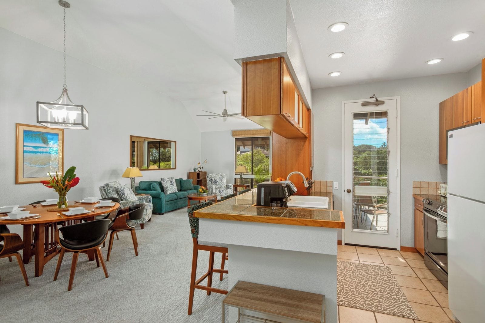 A modern kitchen with a central island, a dining area with a round table, and a living room with a sofa and chairs.