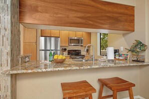 Eine Küche mit Holzausstattung, Edelstahlgeräten und Granit Arbeitsplatten, inklusive zwei hölzerner Barhocker.