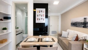 Un salon moderne avec un canapé, une table à manger dressée pour deux personnes et une cuisine en arrière-plan.