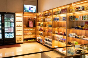 A hotel lobby with a beverage refrigerator, shelves stocked with snacks and toiletries, and a television mounted on the wall.