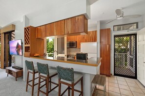 Una cocina moderna con armarios de madera, una barra con taburetes, televisor integrado y vistas al exterior.