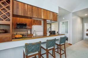 Une cuisine moderne avec des meubles en bois, un four encastré et un évier en acier inoxydable. On y trouve trois tabourets de bar avec des assises en osier tressé.