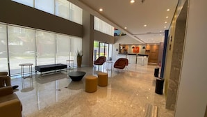 Eine großzügige Lobby mit hoher Decke, großen Fenstern und einer Sitzecke mit modernen Sesseln und Poufs.