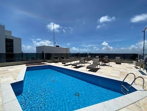 Une piscine sur le toit, avec des chaises longues et un ciel dégagé.
