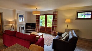 A living room with a red sofa, a black sofa, a television, a fireplace, and a window with curtains.
