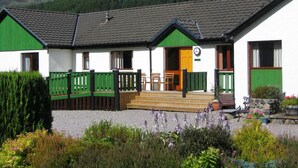 A building with a green and white exterior, a wooden porch, and a mountain backdrop.